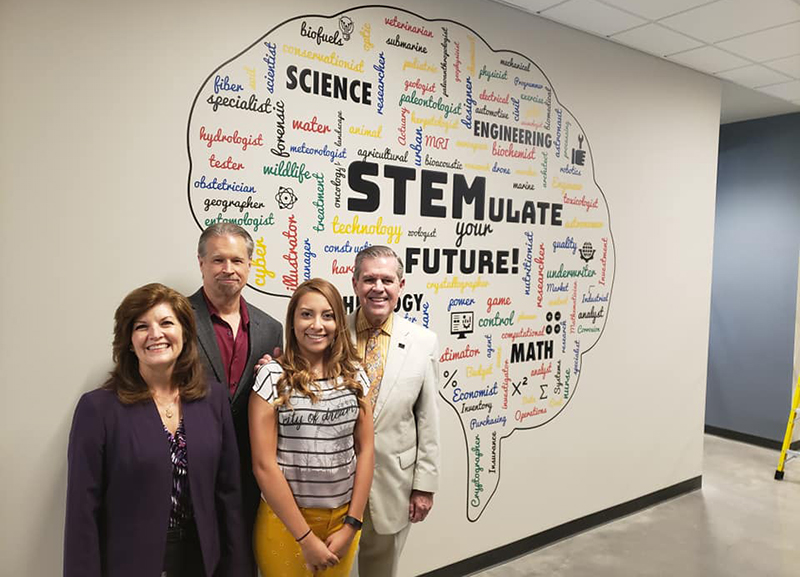 HCC officials and a student pose for photo in front of a STEM mural.